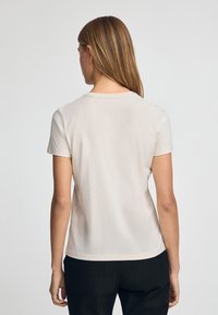 Lichtbeige t-shirt met korte mouwen, gemaakt van zachte stof, met een ronde halslijn en een slim fit ontwerp, gecombineerd met donkere broek.