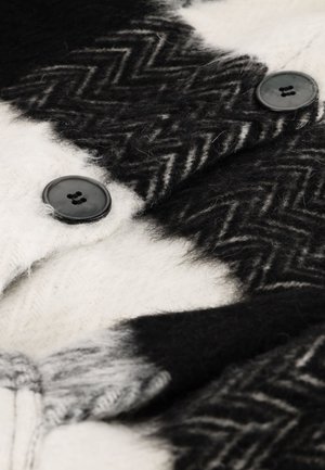 Zwart-witte wollen stof met zigzagpatroon, twee zwarte knopen en een zachte, pluizige textuur.