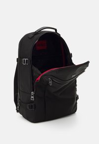 Sac à dos noir en tissu résistant avec intérieur rouge, doté de plusieurs compartiments zippés et de bretelles réglables.