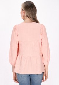 Ferskenfarvet bluse med tekstur, samlet i bunden, lange pufærmer og rund halsudskæring, parret med bløde blå jeans.