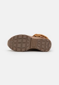 Chaussures marron avec semelle en caoutchouc texturé, présentant un motif en relief pour une meilleure adhérence et un accent en fourrure douce. Semelle conçue pour la durabilité et le confort.
