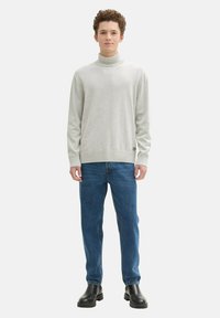 Hellgrauer Rollkragenpullover mit geripptem Saum, getragen mit blauen Jeans und schwarzen Ankle-Boots. Einfaches, minimales Design, glatte Textur.