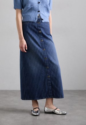 Denim-maksihame, jossa on valkoiset pystysuorat raidat, etupainikkeet ja pehmeä vyötärö. Yhdistetty kiiltäviin hopeisiin tasapohjaisiin kenkiin.