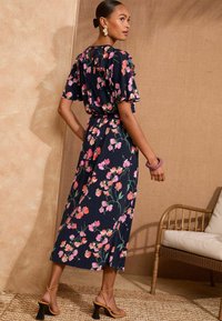 Cvjetna haljina s tamnoplavom pozadinom i ružičastim te zelenim uzorcima. Kratki volanasti rukavi, strukiran struk i lepršav dizajn suknje.