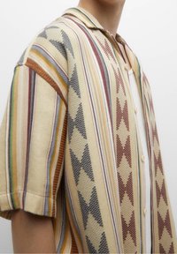 Camicia a maniche corte beige con strisce multicolori e motivi a diamante, realizzata in tessuto testurizzato con chiusura frontale a bottoni.