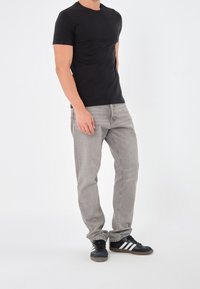 T-shirt nera a maniche corte abbinata a jeans grigio chiaro e sneakers nere con strisce bianche. Design semplice con una silhouette aderente.