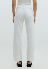 Witte wijde broek met een rafelige tailleband en twee achterzakken, gecombineerd met zwarte platform sandaal. Glad denim textuur.
