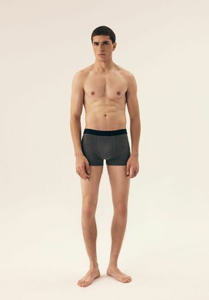 Dark gray boxer shorts with a black waistband, fitted design, and smooth texture, worn by a standing male model against a plain background.