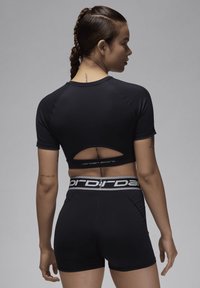 Svart treningstopp med utskjært rygg, parret med svarte shorts. Har en kontrasterende midje med logoakkenter. Glatt, tettsittende tekstur.