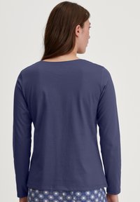Paarse blouse met lange mouwen en een ronde halslijn, gemaakt van zachte stof. Eenvoudig ontwerp zonder patronen, met zichtbare stiksels langs de zoom.