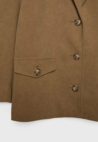 Blazer en daim marron avec un col cranté, quatre boutons et une poche à rabat avec fermeture à bouton. Texture lisse avec une coupe cintrée.