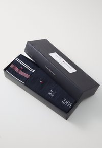 Dos pares de calcetines azul marino en una caja negra, con un par de diseño a rayas y el otro con texto, ambos con acentos de logo.