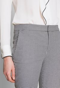 Svart och vit hounds-tooth mönstrade byxor med fickor, skräddarsydd passform och en slät textur, i kombination med en krämf ärgad blus med svarta accenter.
