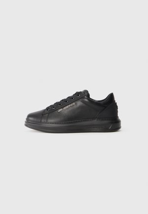 Black leather sneaker with a round toe, flat sole, and lace-up design. Features logo accents and smooth texture. Side view presented.
