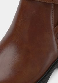 Rudos odinės ankle batai su lygiu paviršiumi, apvalia nosimi ir elastingais šonais. Juoda guminė padas su griovelių krašto detale.