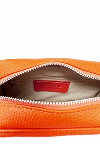 Bolso de piel naranja con superficie texturizada. Cierre de cremallera con dientes plateados, que revela un interior beige y una pequeña etiqueta roja en su interior.