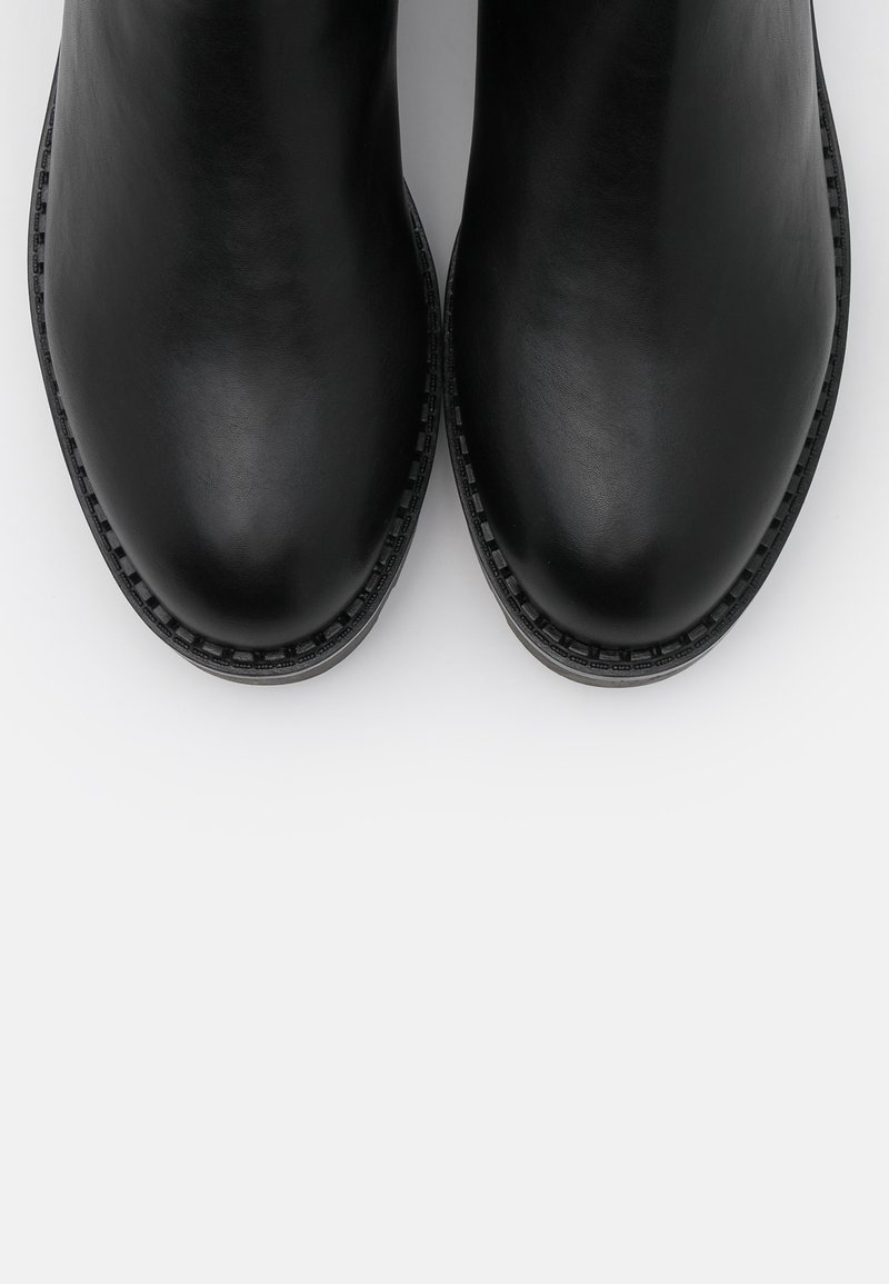 Stivali neri in pelle alla caviglia con finitura liscia, punte arrotondate e cuciture decorative lungo i bordi, posti su uno sfondo bianco.