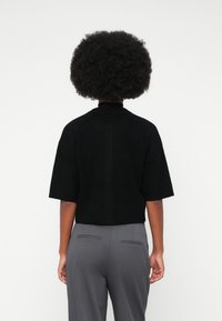 Black cropped sweater with short sleeves, textured fabric, high neck, paired with gray tailored pants featuring back pockets.