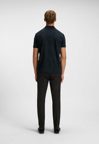 Svart kortärmad polo med en subtil strukturerad mönster, kombinerad med svarta byxor, med klassisk krage och rak nederkant.