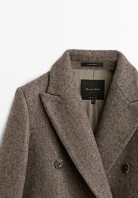 Brun stof blazer med tekstureret finish, spidse klapkraver og dobbeltbrystet front. Har to runde knapper og en sort label indeni.