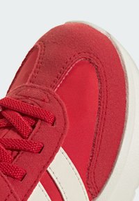 Červené tenisky vyrobené z kombinácie semišu a sieťoviny, s textúrovanými detailami a bielymi akcentmi po stranách. Okrúhla špička a šnurovací dizajn.