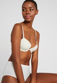 Light beige bra with lace trim and adjustable straps, paired with high-waisted white briefs. Smooth texture, simple design, and clean lines.