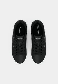 Zapatillas negras con un acabado de cuero texturizado, con cordones negros, una suela de goma blanca y un logo de Champion en la lengüeta.