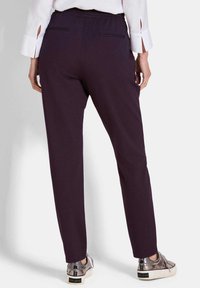 Lila, dehnbare Hosen mit elastischem Bund und Rückentaschen, kombiniert mit metallischen Sneakern mit strukturierten Akzenten.