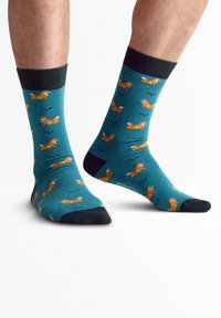 Calcetines turquesa con patrones de zorros naranjas, puños acanalados negros y acentos negros en el talón y la punta. Adecuados para uso casual.