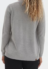 Šedý pletený svetr s dlouhými rukávy, texturovaná tkanina, žebrované manžety a spodní lem, s malou značkovou nálepkou na spodní straně.