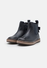 Bottines en cuir noir avec des panneaux élastiques sur les côtés, des bords festonnés, une languette de tirage et une semelle contrastante cousue en marron. Fini doux et bout arrondi.