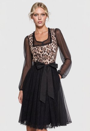 Woman wearing a dress with sheer black long sleeves, a leopard print bodice, a square neckline, and a black lace skirt tied with a wide black bow.