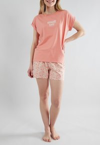 Korte mouwen, koraalkleurig T-shirt met de tekst "Great Day", gecombineerd met perzikkleurige shorts met bloemmotief. Zachte katoenstof met een comfortabele pasvorm.