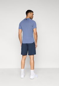 Αθλητική στολή με εφαρμοστό μπλε κοντομάνικο μπλουζάκι και ναυτικά σορτς, συνδυασμένη με λευκά αθλητικά παπούτσια και κάλτσες μήκους έως τον αστράγαλο.