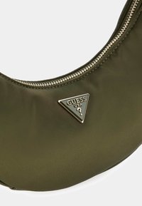 Borsa in nylon verde oliva dalla forma arrotondata, con una cerniera argento e un logo metallico triangolare ben visibile con la scritta "GUESS USA".
