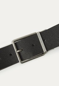 Schwarzer, strukturierten Leder Gürtel mit einer silbernen Metallschließe, die rechteckig geformt ist und mehrere Einstelllöcher aufweist. Mit "Calvin Klein" gekennzeichnet.