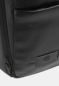 Zaino in pelle nera con superficie texturizzata, chiusura a zip e tasca frontale. Presenta un piccolo logo impresso e un design elegante e moderno.