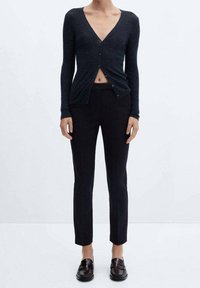 Donkerblauwe geribbelde cardigan met een diepe V-hals en knoopsluiting, gecombineerd met strakke zwarte broeken en donkere instappers.