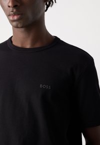 Juodas trumpo rankovėmis marškinėliai iš tekstūruotos medžiagos, su stangriu kaklu ir subtiliu, toniniu "BOSS" logotipu krūtinėje.