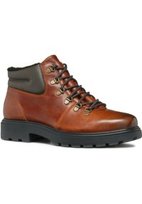 Stivale da trekking in pelle marrone con un collo imbottito grigio, occhielli in metallo, lacci scuri e una suola in gomma nera con un motivo di battistrada robusto.