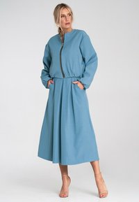 Niebieska sukienka z długimi rękawami, okrągłym dekoltem i zapięciem na zamek, z bocznymi kieszeniami i plisowanym dołem, wykonana z gładkiego materiału.