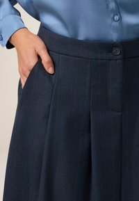 Pantaloni navy a righe con un tessuto texturizzato, caratterizzati da una piega frontale, tasche laterali e una chiusura a bottoni in vita.