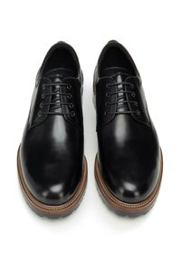 Czarne skórzane buty o gładkim wykończeniu, zaokrąglonych noskach, sznurowane, z brązowymi gumowymi podeszwami z teksturowanym wzorem.