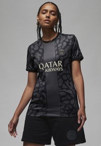 Musta urheiluasu mattapinnalla, jossa on leopardikuvio. Kultaiset tekstit lukevat "Qatar Airways" yhdistettynä mustiin shortseihin.