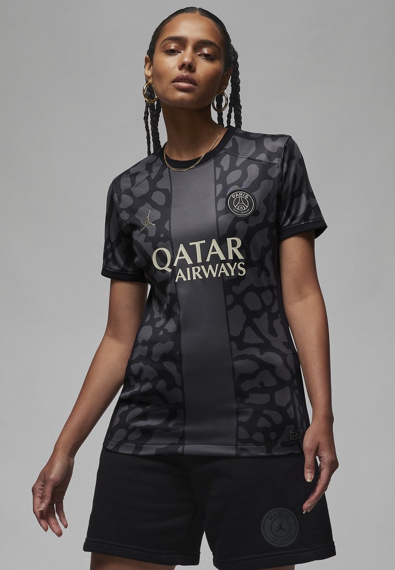 Musta urheiluasu mattapinnalla, jossa on leopardikuvio. Kultaiset tekstit lukevat "Qatar Airways" yhdistettynä mustiin shortseihin.