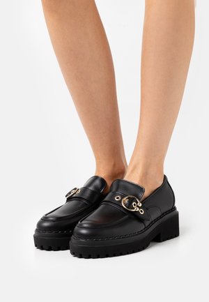 Sorte læder loafers med tykke, teksturerede såler. Har en spænde i guldfarve, glat overflade og et rundt tådesign.