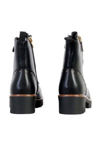 Bottines en cuir noir avec des zips dorés, des clous en bronze le long du talon et un talon noir empilé. La vue arrière met en valeur les caractéristiques du design.