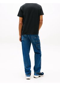 Svart bomull t-shirt och blå denimbyxor. Lätta jeans med fickor och subtilt blekning. Sneakers i marinblått och vitt fulländar looken.