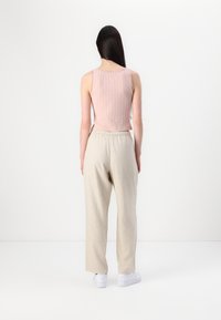 Top roz deschis cu dungi, purtat cu pantaloni bej cu aspect de in, având un talie elastică și adidași albi, văzut din spate.