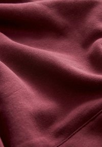 Tissu bordeaux lisse et plié avec des coutures visibles et un jeu subtil de lumière et d'ombre sur sa surface texturée.